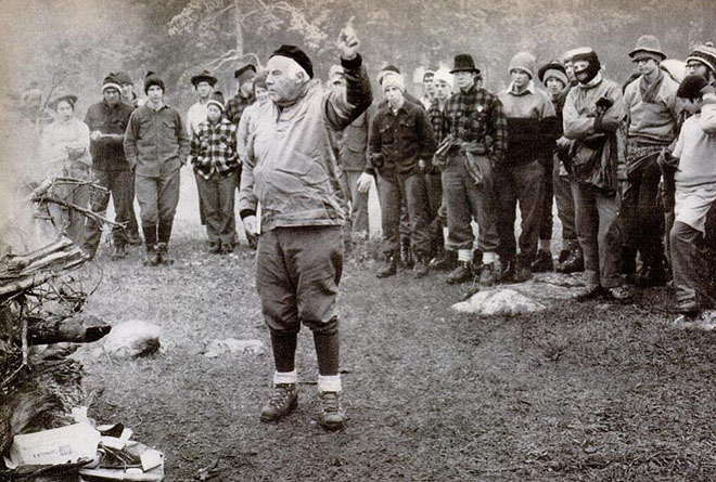 Black-and-white archival photo of Paul Petzoldt, arm raised, teaching a group of students in wool clothing outdoors