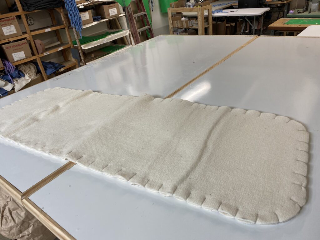 Bare cream wool felt sleeping pad with scalloped stitched edges lying on a large white cutting table in the Lucky Sheep workshop