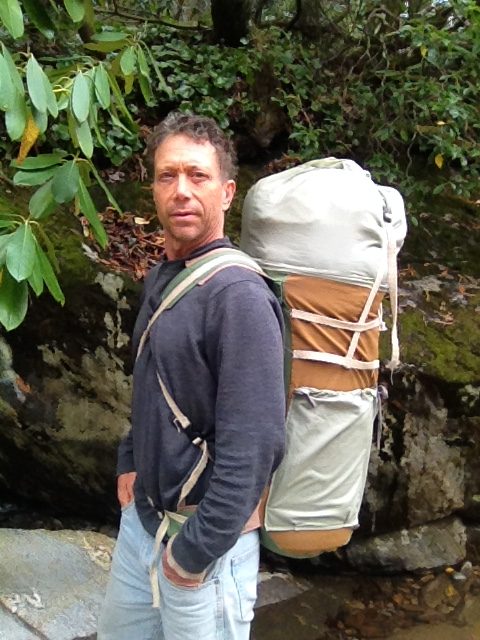 Patrick beside a mossy creek wearing a large canvas pack with a wool bedroll strapped on