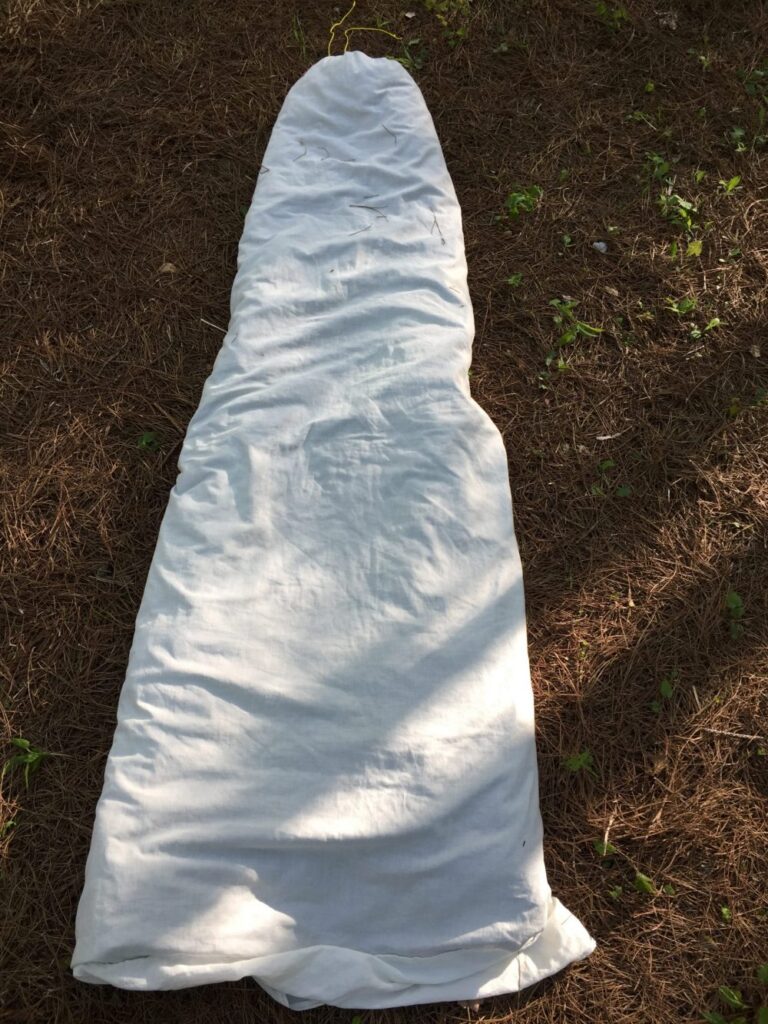 White tapered sleep sack laid on a bed of pine needles, drawcord closure at the head end, viewed from above