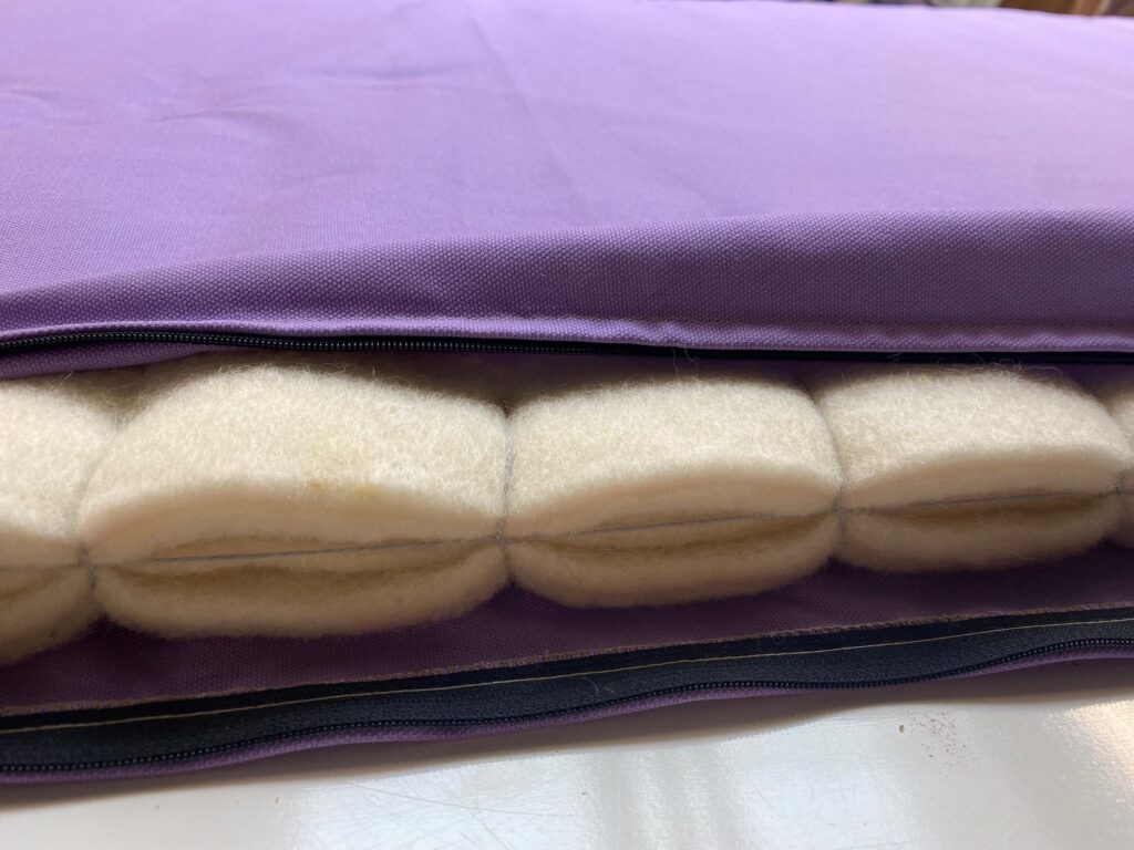 Close-up of a wool sleeping pad in a purple organic cotton cover with the zipper open, showing six thick layers of cream wool felt inside